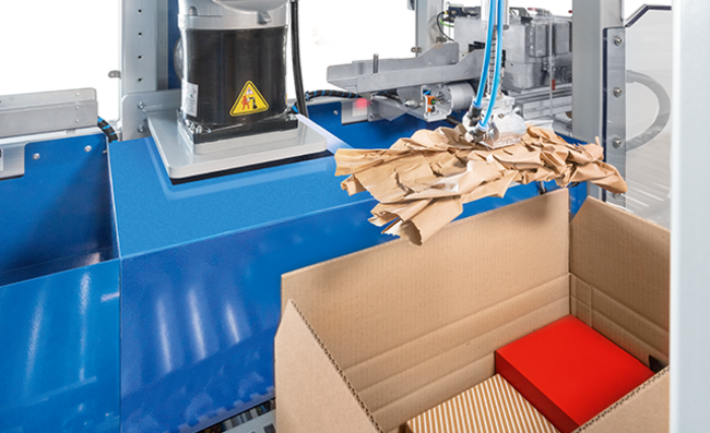 A paper cushion is placed fully automatically in a box containing goods for shipment.